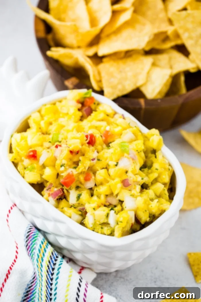 A pristine white pineapple serving dish showcases a generous portion of fresh pineapple salsa, rich with colorful peppers, aromatic cilantro, and finely diced red onions.