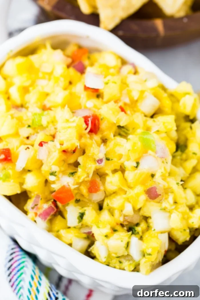 A pristine white pineapple serving dish showcases a generous portion of fresh pineapple salsa, rich with colorful peppers, aromatic cilantro, and finely diced red onions.