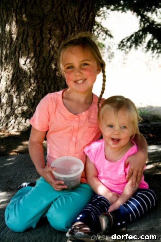 Two young girls playing near tree branches that form natural forts, capturing a moment of childhood wonder