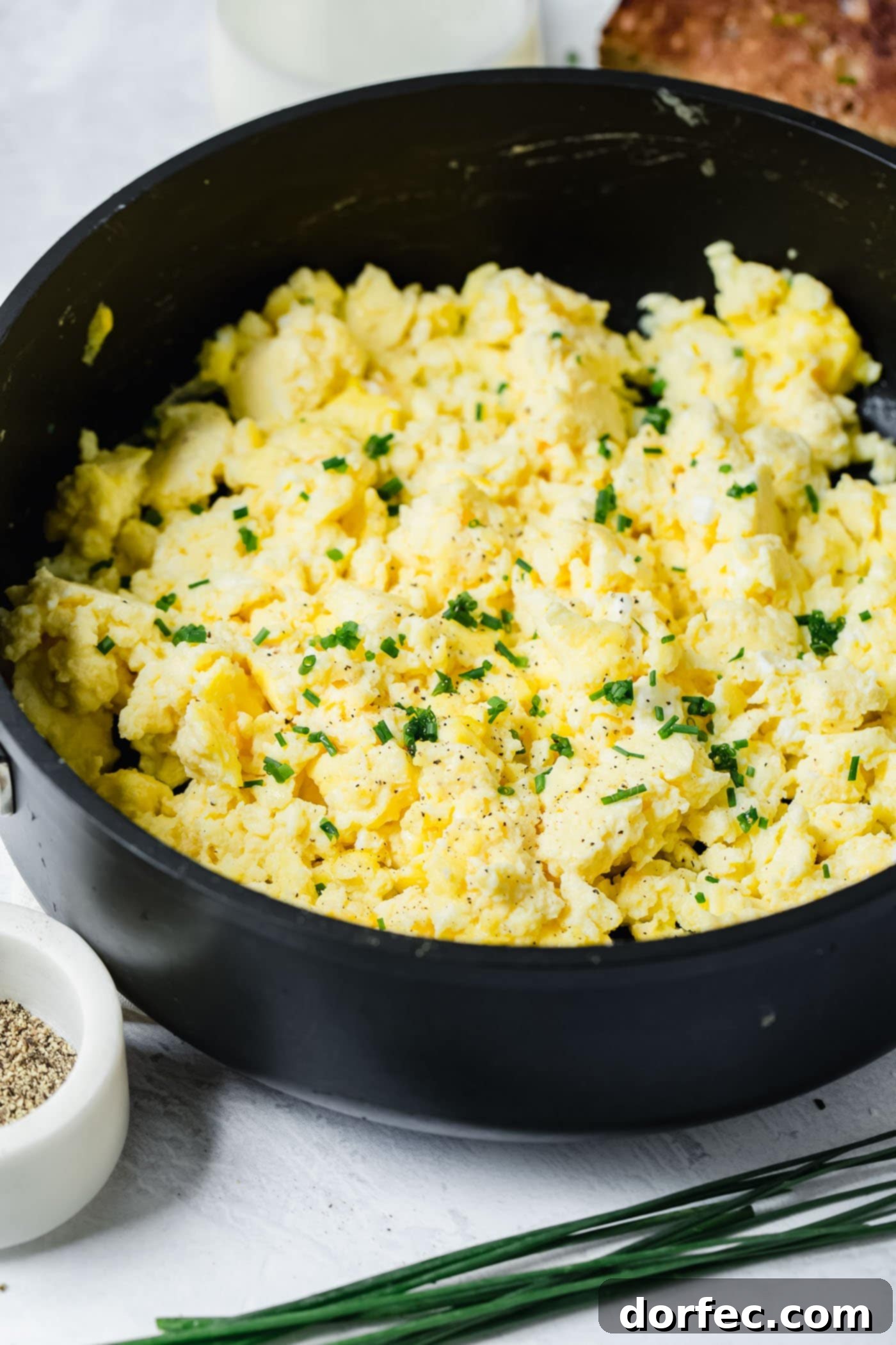 Serving Perfect Scrambled Eggs A sleek black bowl brimming with fluffy scrambled eggs, delicately sprinkled with vibrant slices of fresh green onion for a touch of color and flavor.
