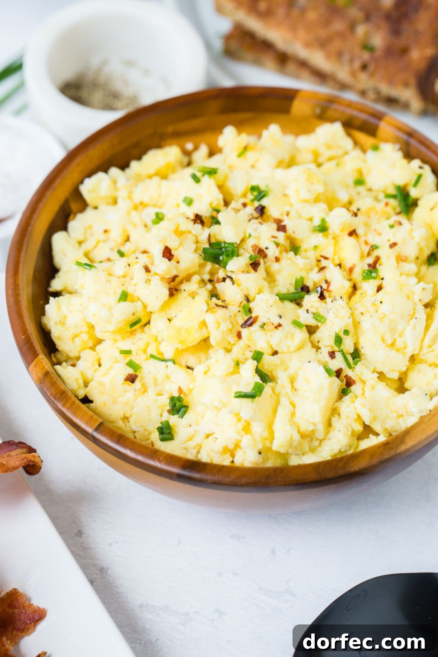Garnished Scrambled Eggs A wooden bowl of beautifully scrambled eggs, generously sprinkled with vibrant green onion slices, ready to be enjoyed.