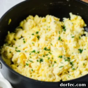 A close-up of a bowl of fluffy scrambled eggs, topped with fresh chives, indicating a perfect texture.