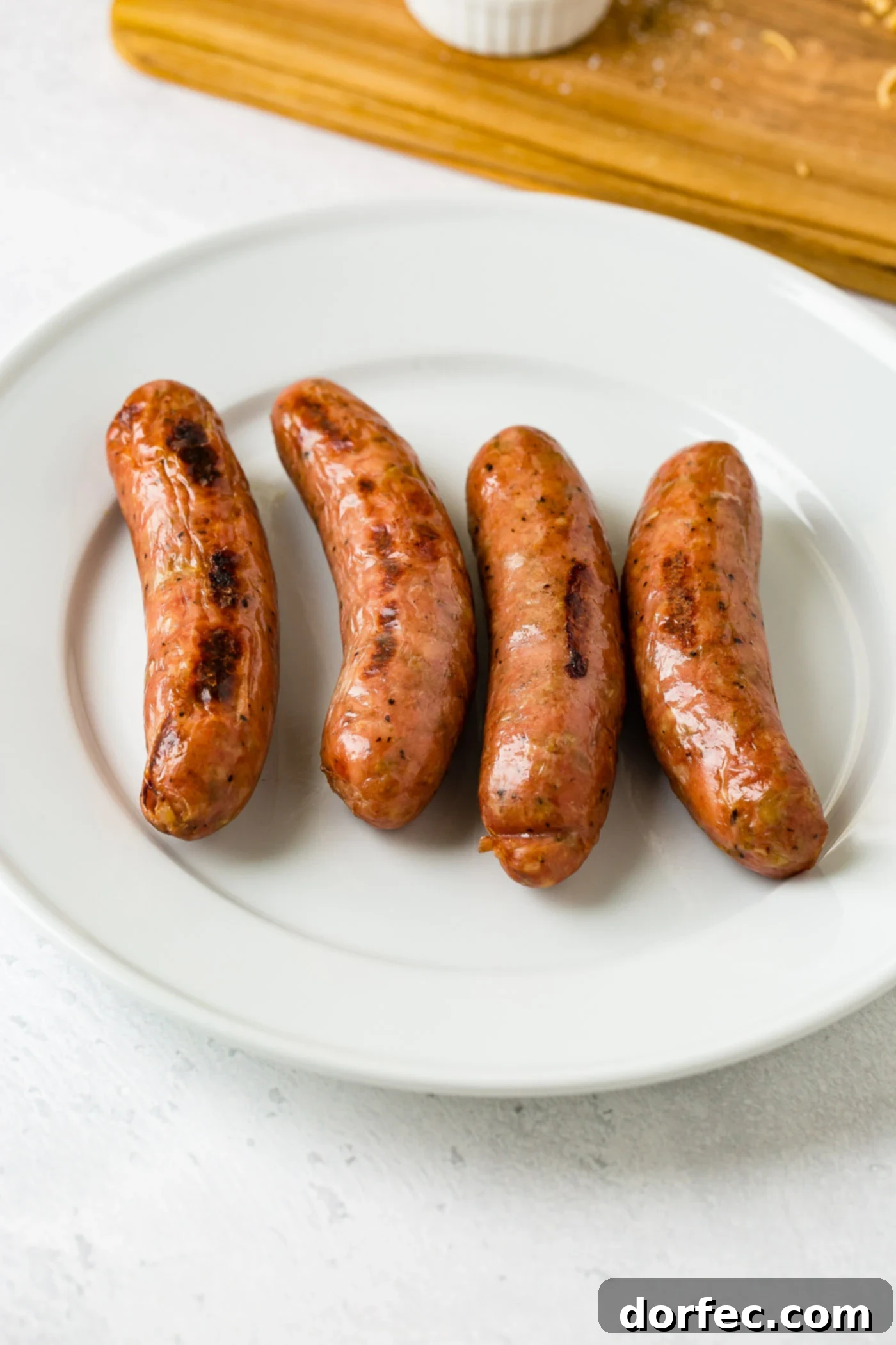 Four apple chicken sausages on a white plate.