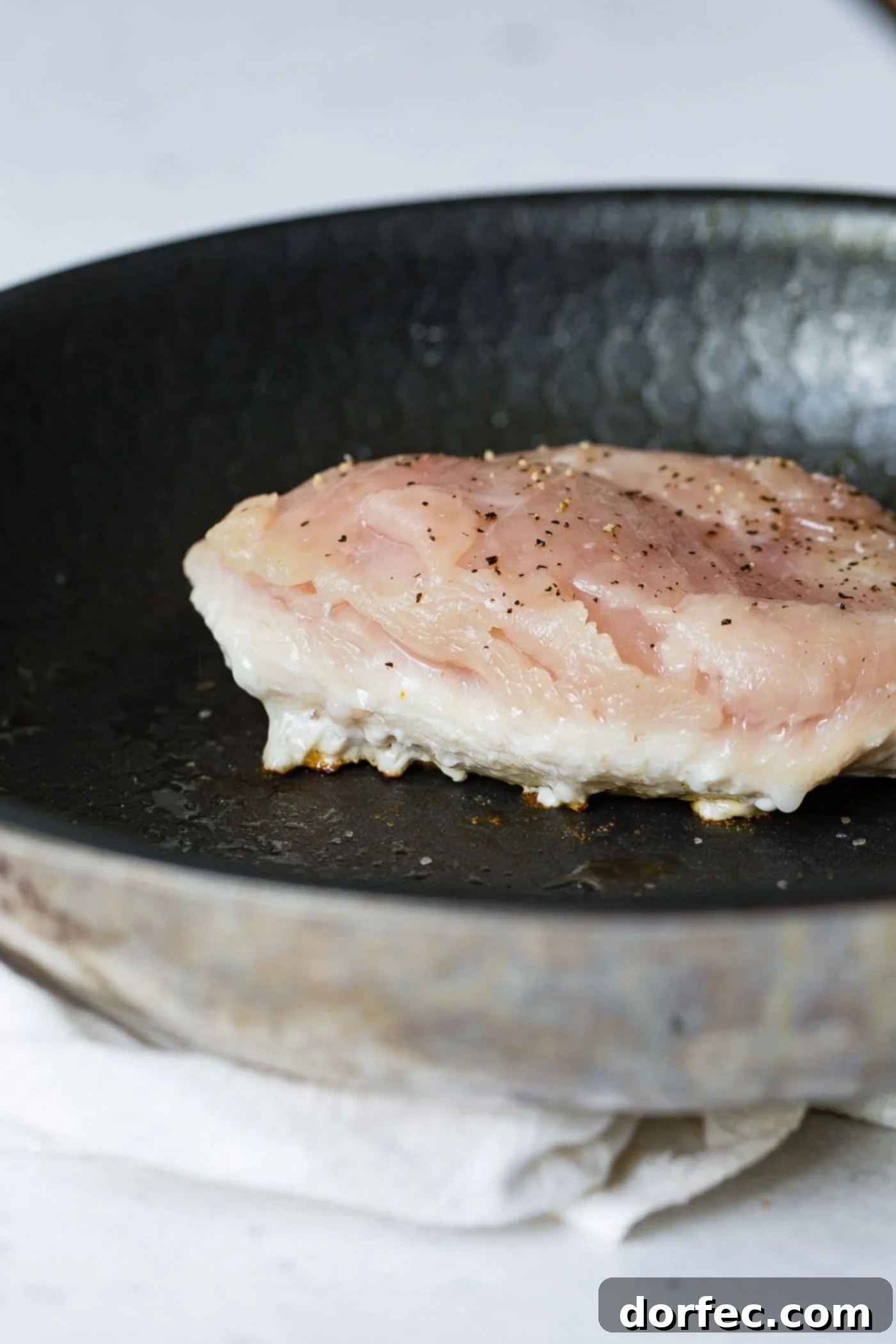 Pan-Seared Chicken Perfection 2 A chicken breast cooking in a skillet. The breast is cooked about half way through.