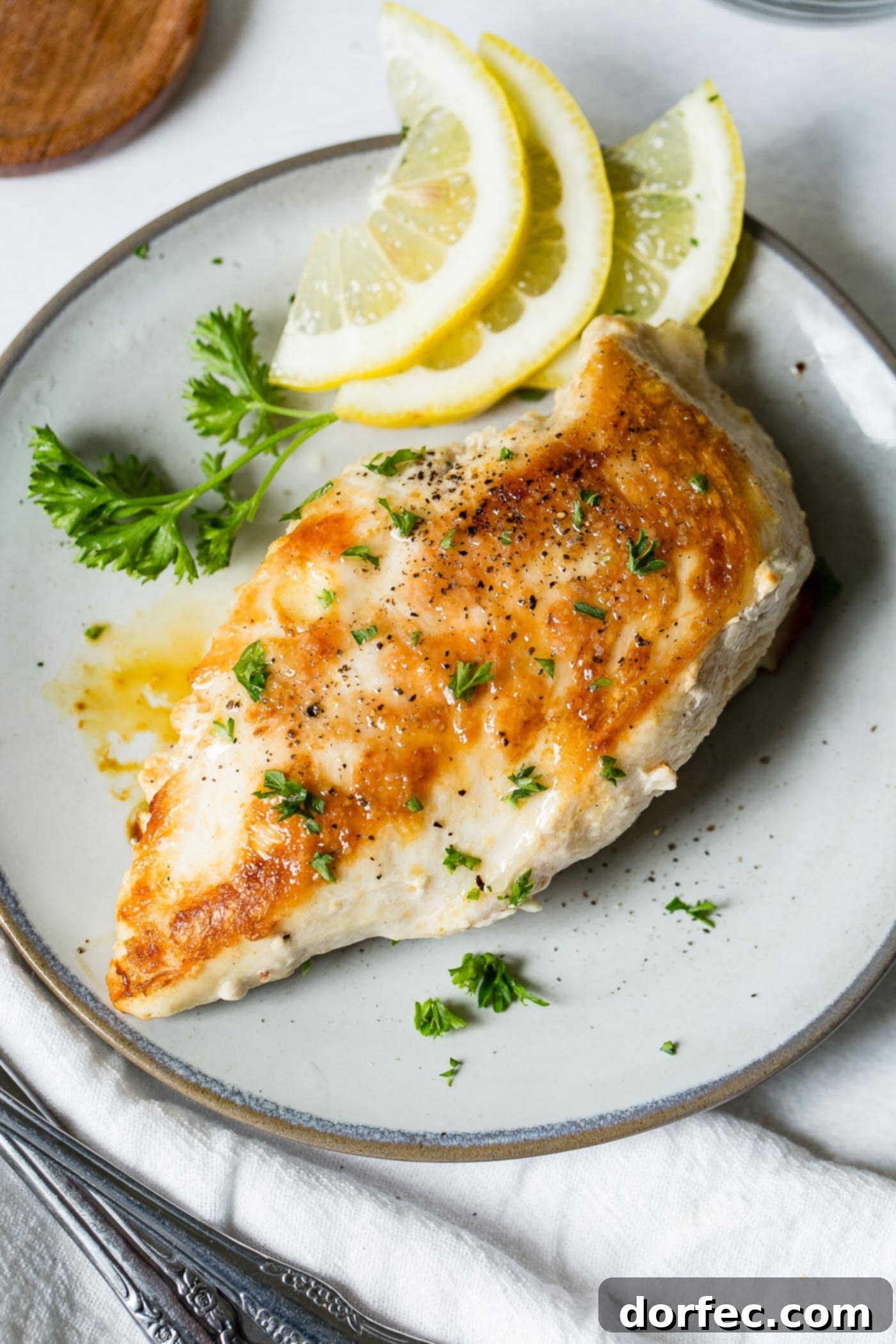 Pan-Seared Chicken Perfection 5 A chicken breast that has been cooked to a perfect golden brown. The breast is on a white plate with lemon slices and a little fresh parsley.