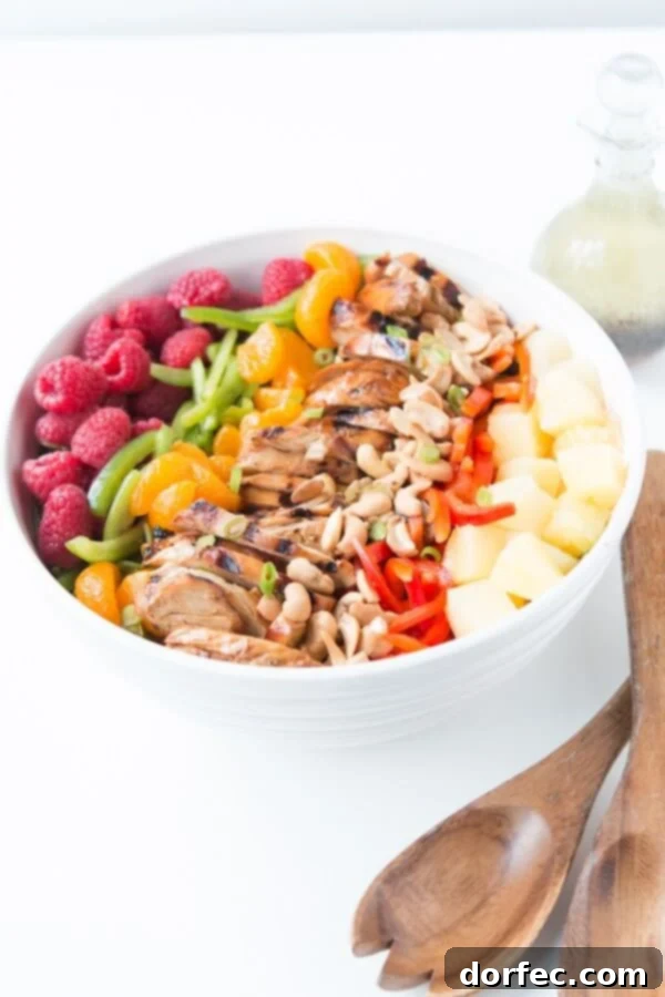 A vibrant bowl of easy teriyaki chicken salad featuring crisp greens, colorful bell peppers, sweet pineapple chunks, and fresh raspberries, elegantly topped with crunchy cashews.