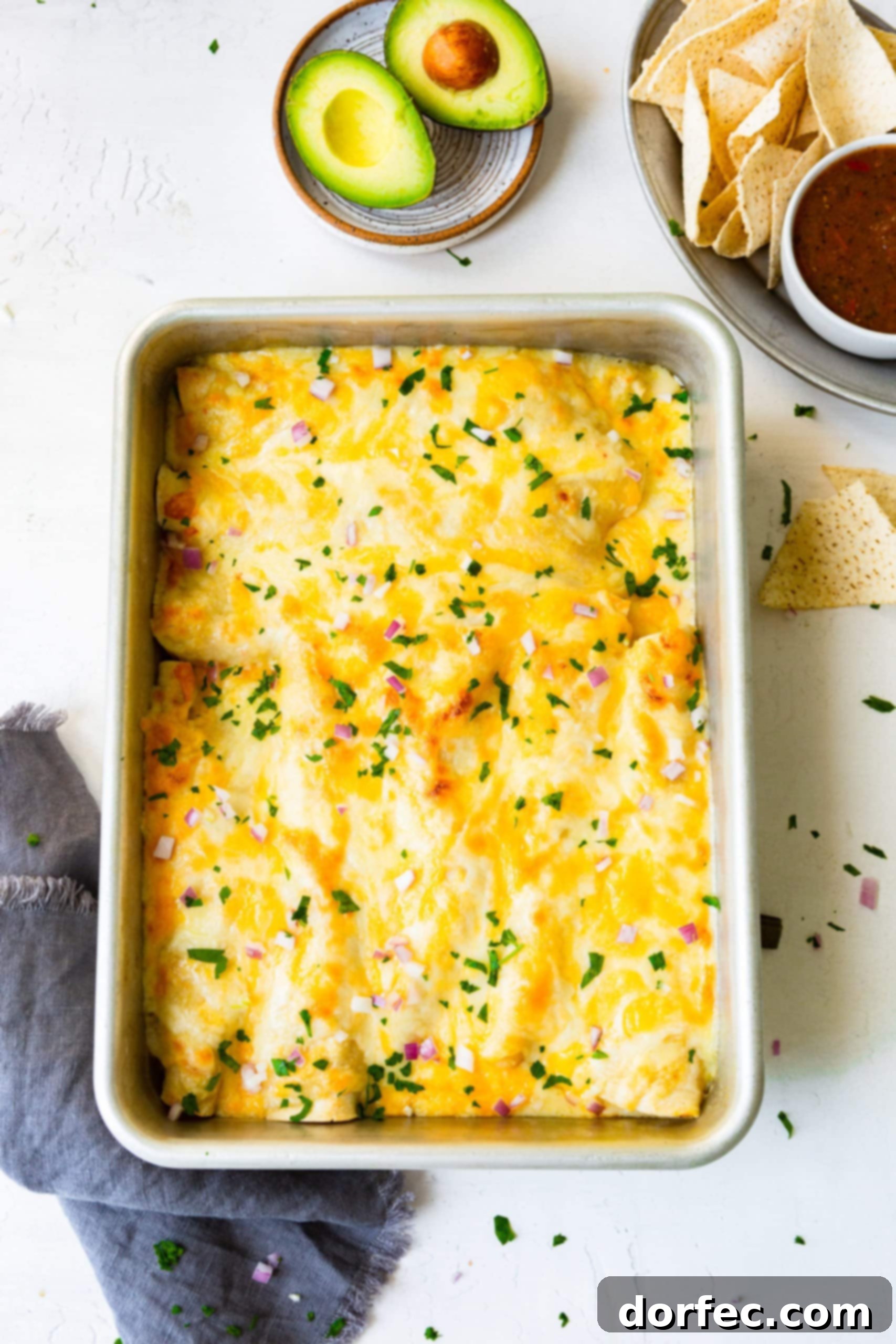 A photo of a 9x13 baking pan filled with golden-brown Honey Lime Chicken Enchiladas, covered in bubbly melted cheese and garnished with fresh chopped cilantro.