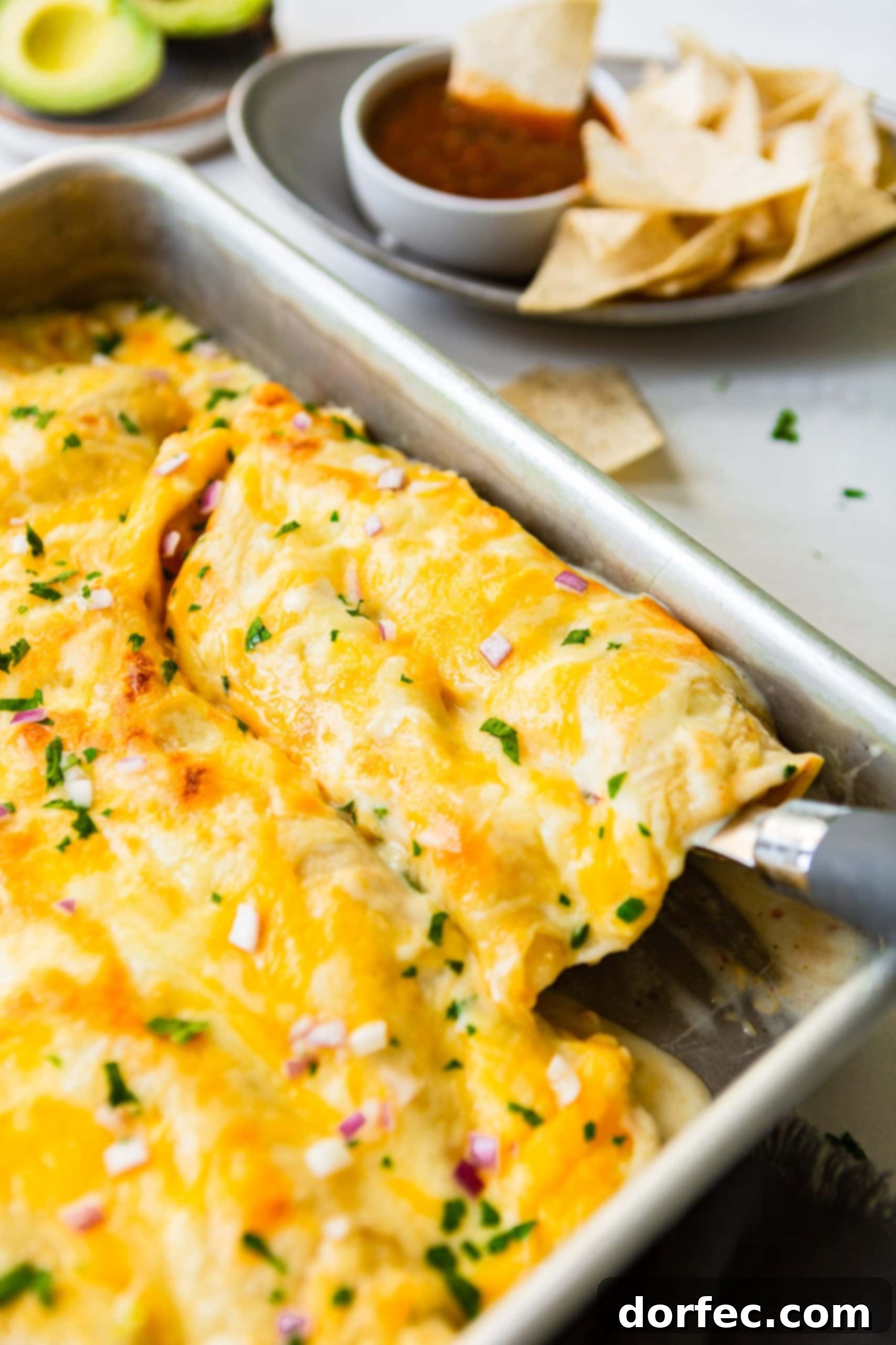A photo of a spatula serving two delicious Honey Lime Chicken Enchiladas from a large baking pan, showcasing the melted cheese and rich sauce.