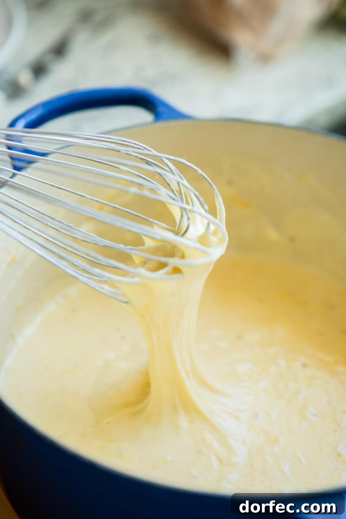 Loaded Chicken Bacon Ranch Macaroni and Cheese 4 Rich cheese sauce for mac and cheese simmering in a vibrant blue Dutch oven, with a whisk resting on top