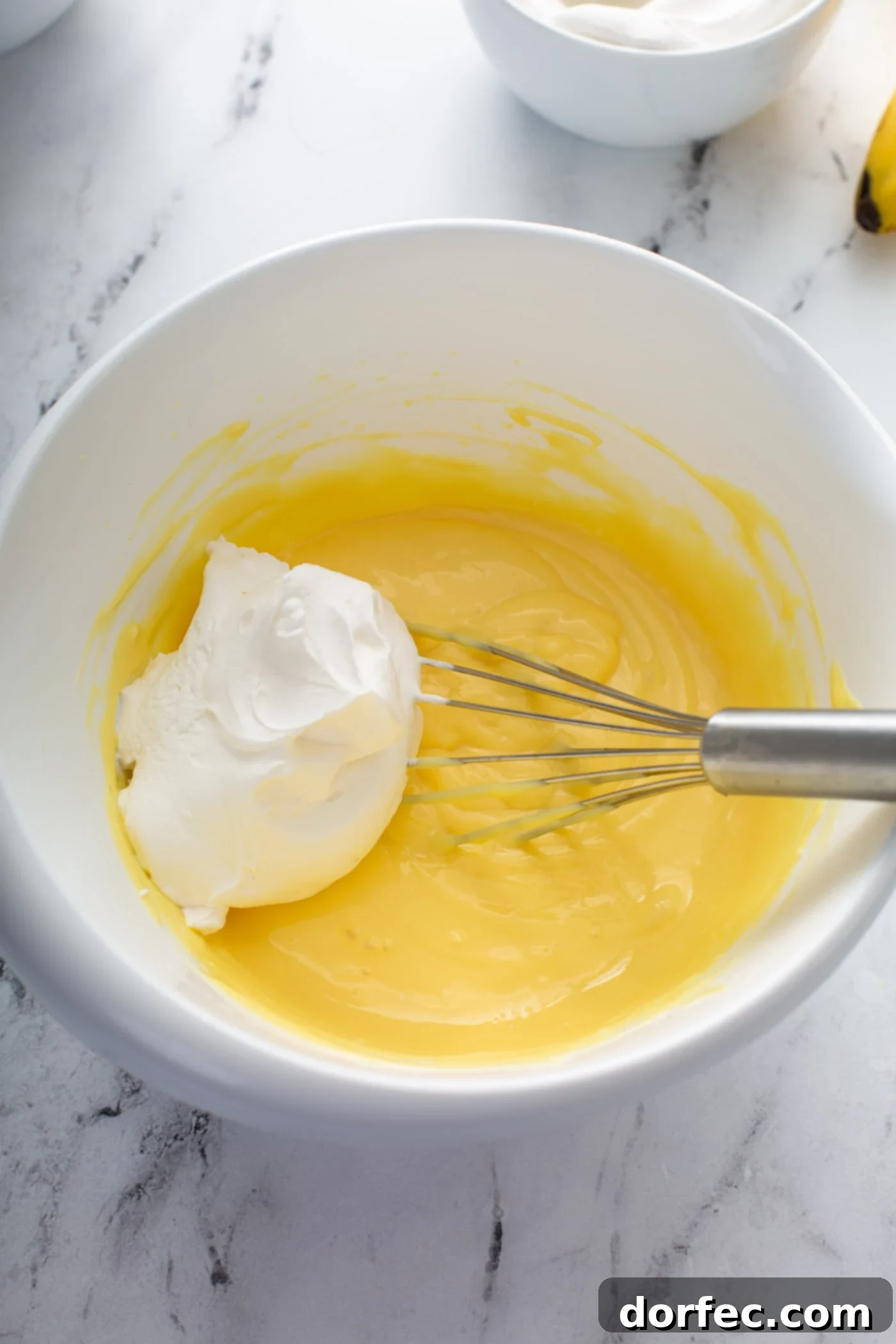Decadent Dulce De Leche Banana Cream Pie 11 Whipped cream on top of the pudding mixture, the cream is being whisked into the mixture.