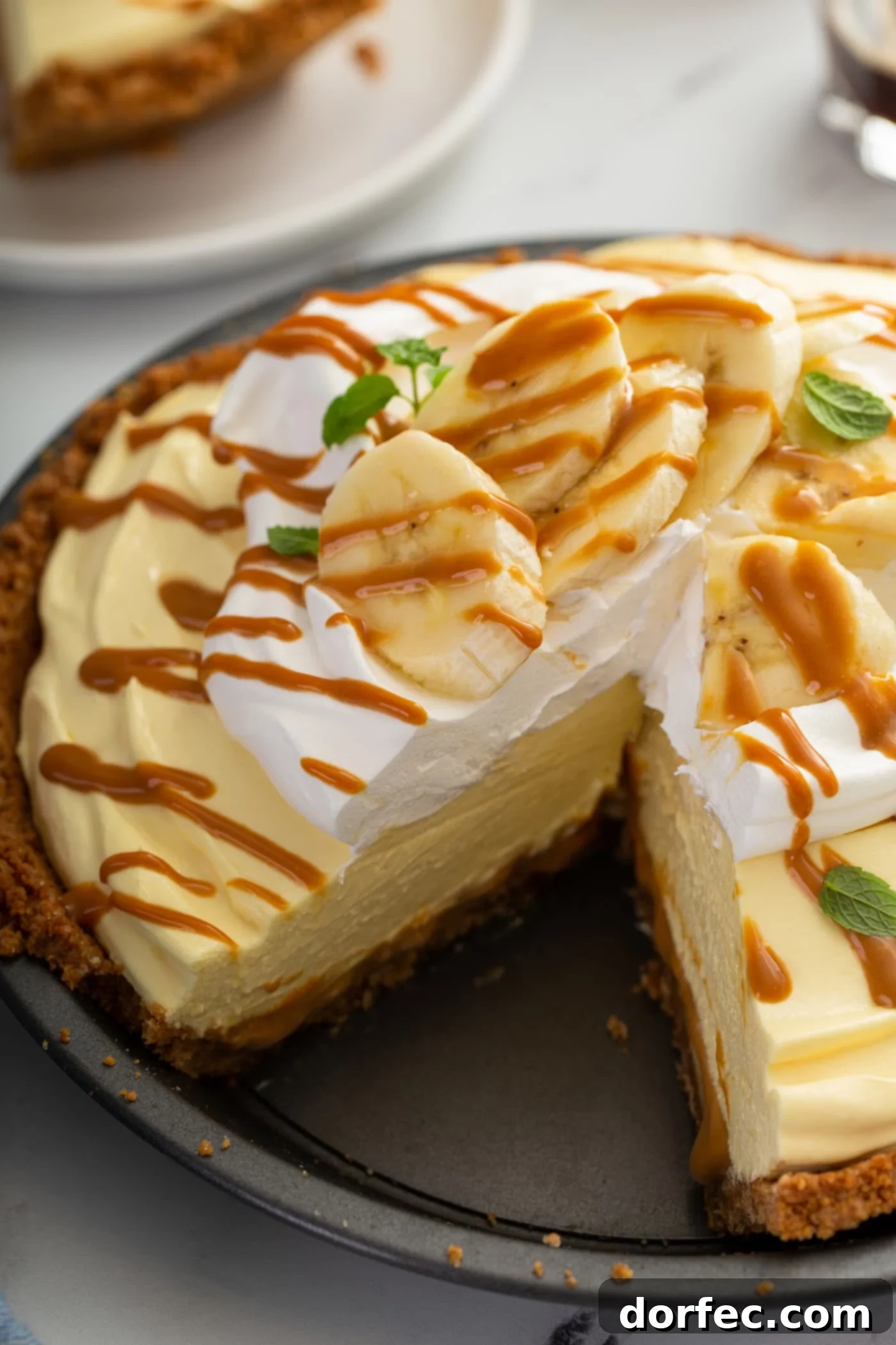 Decadent Dulce De Leche Banana Cream Pie 19 A dulce de leche banana cream pie with whipped cream and sliced bananas on top. The whole pie is drizzled with dulce de leche and a slice has been cut from the pie.