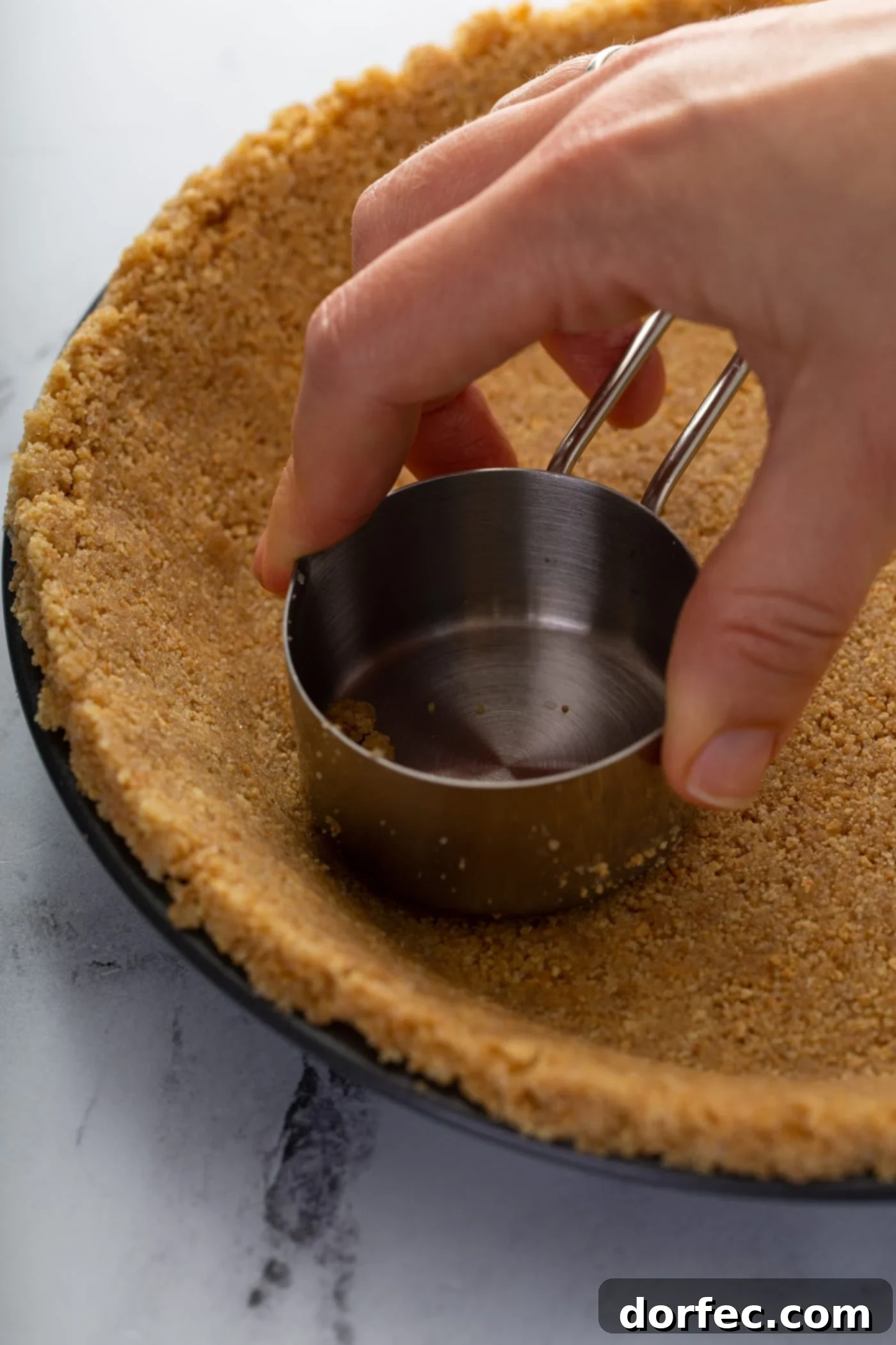 Decadent Dulce De Leche Banana Cream Pie 4 A pie dish with graham cracker crust being pressed into it with a measuring cup.