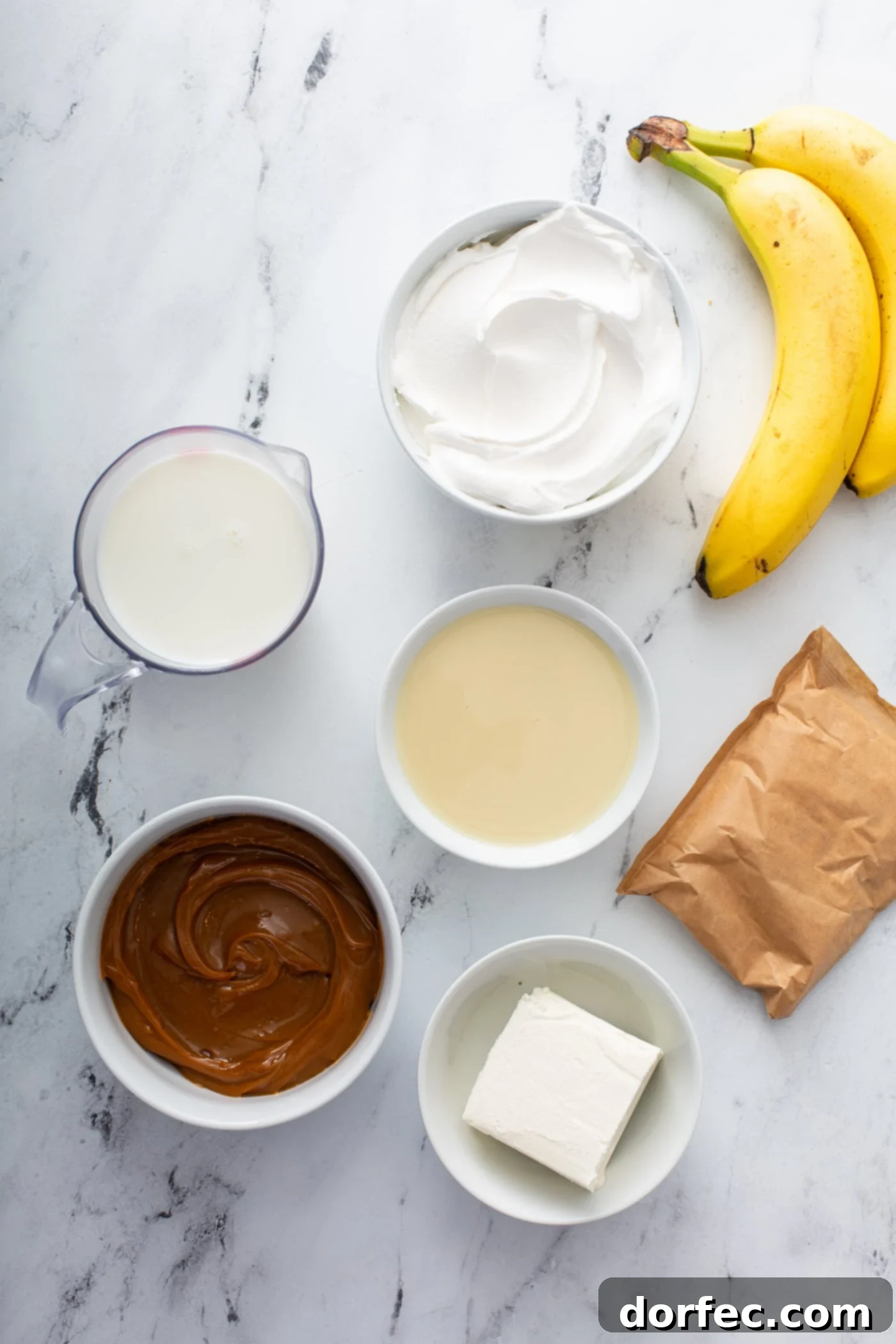 Decadent Dulce De Leche Banana Cream Pie 7 Ingredients for dulce de leche banana cream pie. There are containers of dulce de leche, pudding, milk, cream, sugar, cream cheese and bananas.