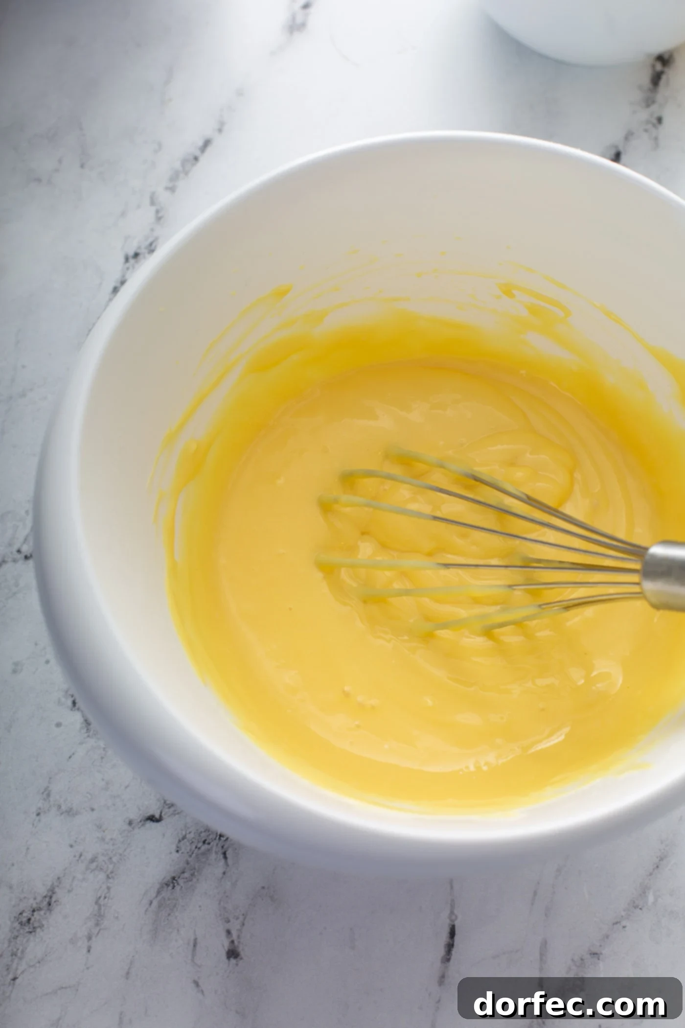 Decadent Dulce De Leche Banana Cream Pie 10 A mixing bowl of pudding and cream cheese. The mixture is being whisked together to a creamy yellow consistency.