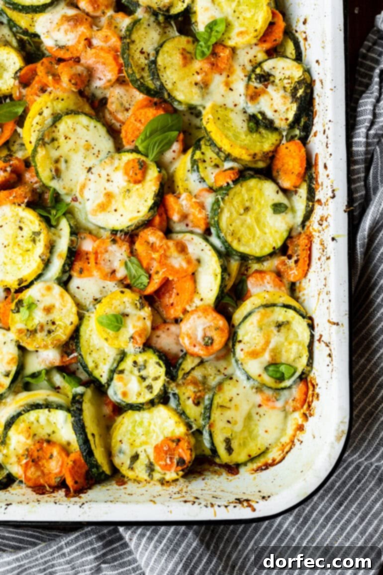 a photo of a white rectangular baking dish full of roasted sliced zucchini, yellow squash and carrots topped with fresh basil and cheese
