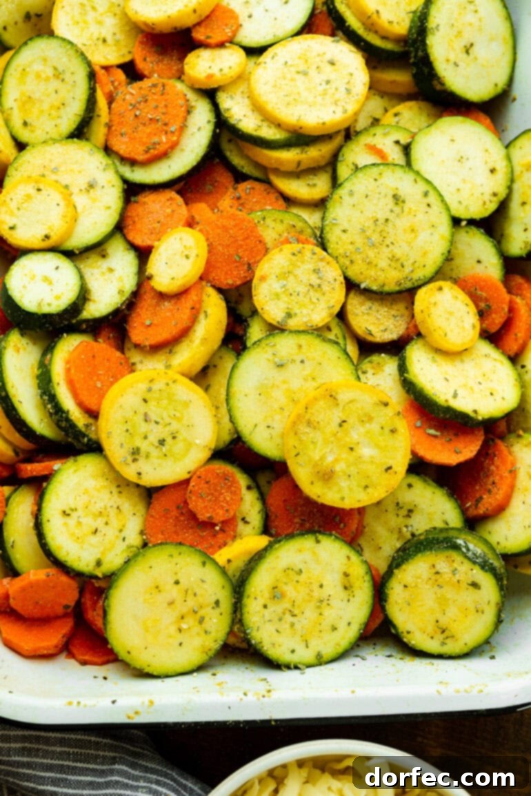a photo of a rectangular baking dish filled with fresh sliced zucchini, yellow squash and carrots ready to be roasted