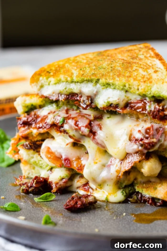 Two stacked sun dried tomato bacon pesto grilled cheese sandwiches with little basil leaves, ready to be enjoyed