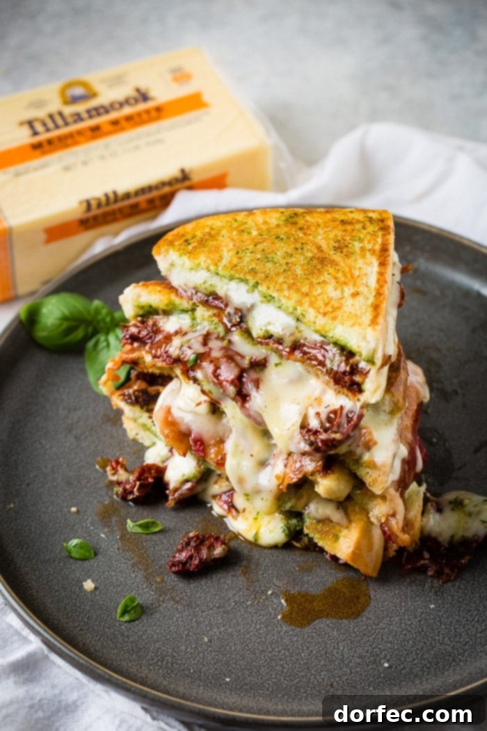 Close-up of a two sun dried tomato bacon pesto grilled cheese sandwich with basil garnish
