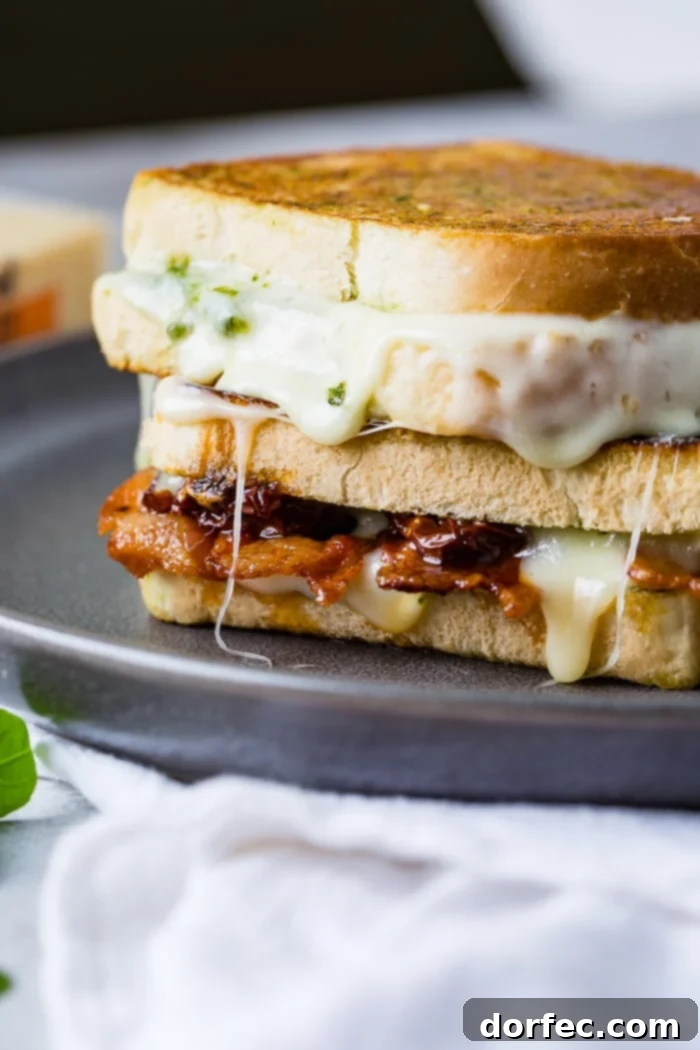 Stacked sun dried tomato bacon pesto grilled cheese sandwiches, showcasing the vibrant filling