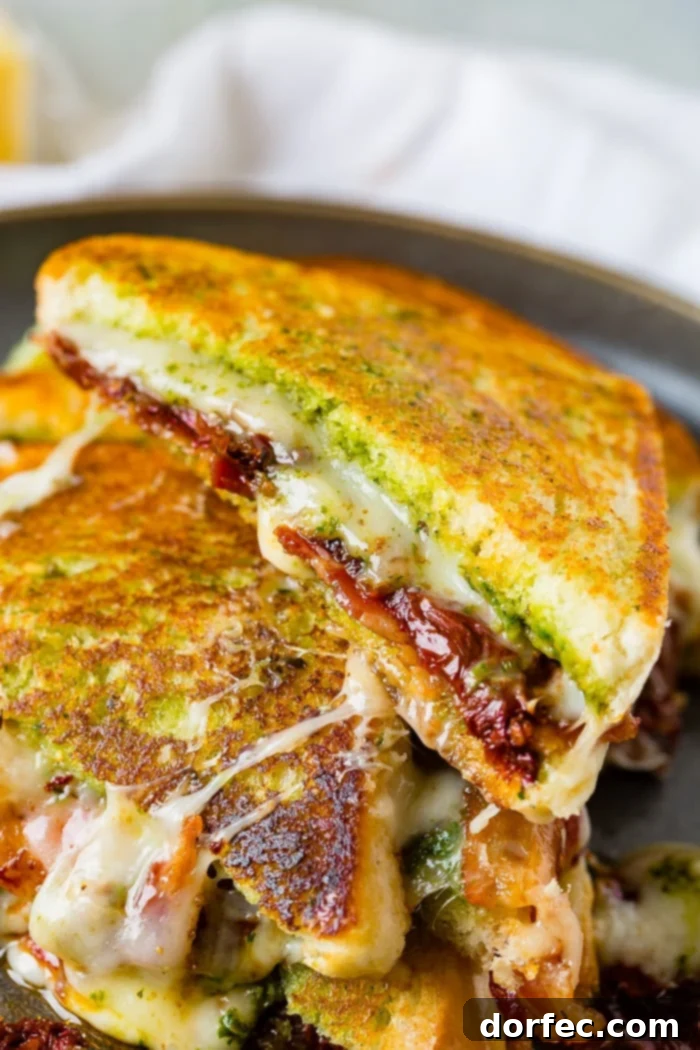 Close up view of two sun dried tomato bacon pesto grilled cheese sandwiches with melted cheese