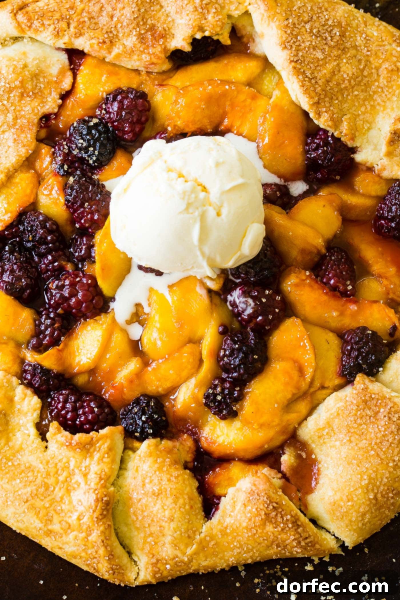 A beautifully rustic peach blackberry galette, brimming with ripe peach slices and dark blackberries, baked in a golden, flaky cornmeal crust on a baking sheet. It's a perfect fall or summer dessert.