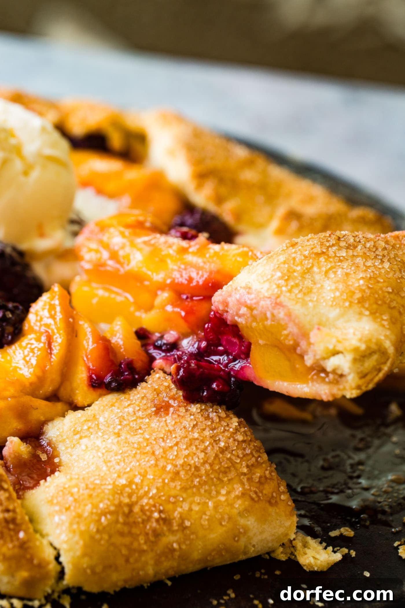 A close-up of the rustic peach blackberry galette, showing the glistening, juicy fruit filling and the golden-brown, folded pastry crust.