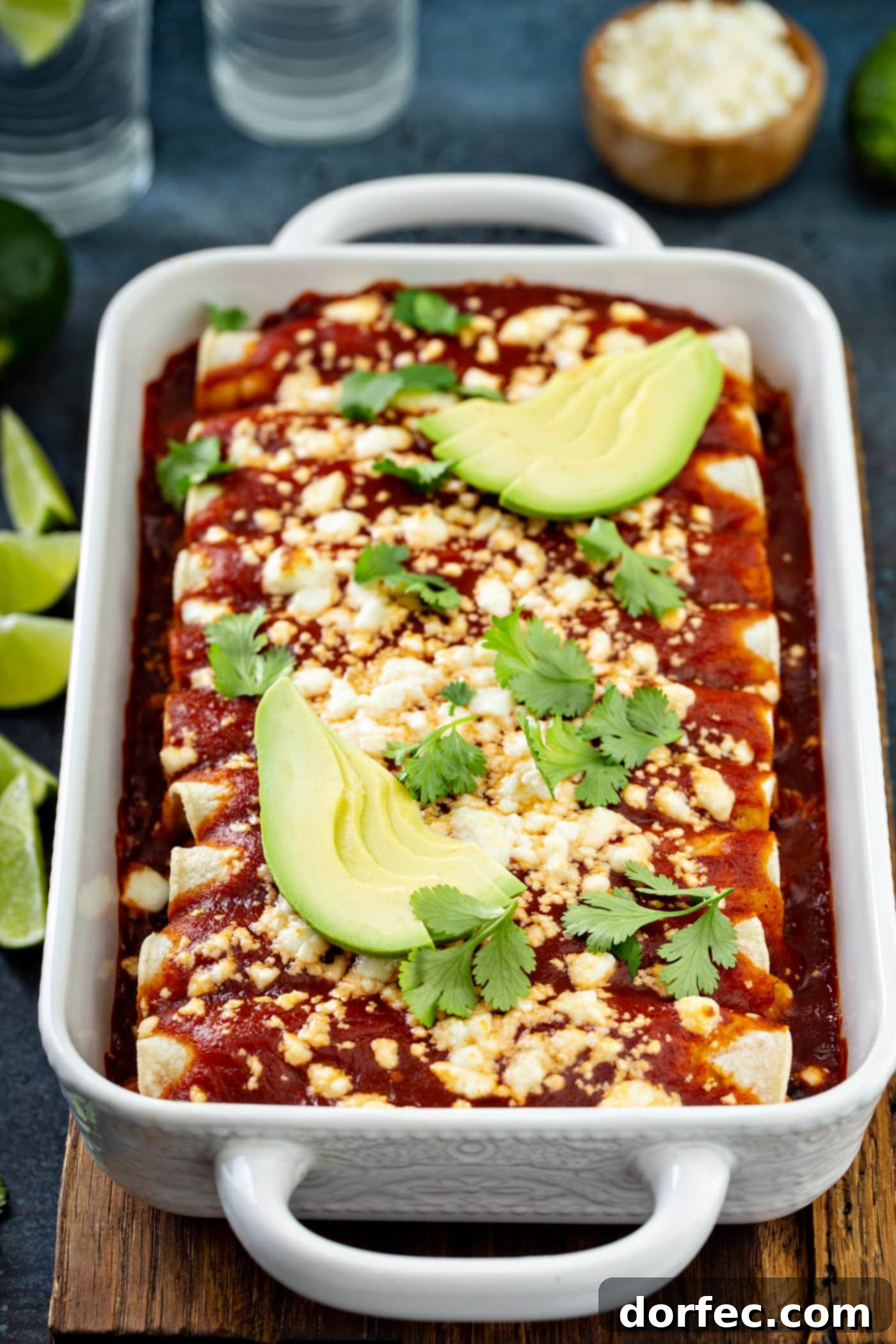 A casserole dish filled with baked sweet potato enchiladas, featuring a rich red sauce, crumbled queso fresco, fresh avocado slices, and cilantro leaves. This inviting vegetarian enchilada dish is ready to be served, highlighting its vibrant colors and healthy ingredients.