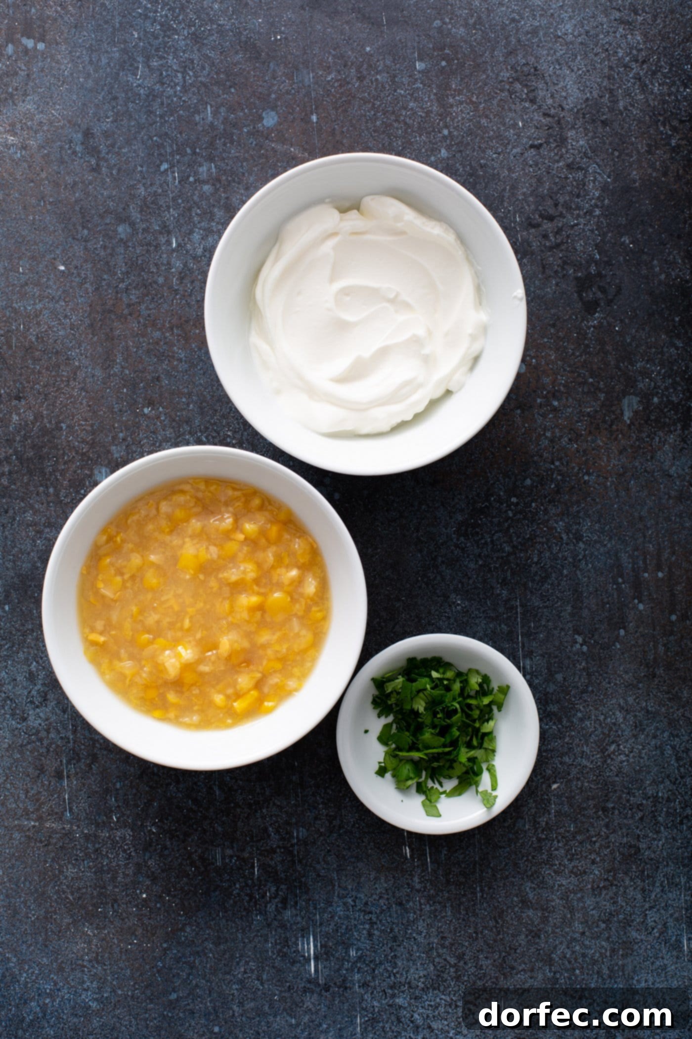 Small bowls containing creamed corn, fresh cilantro, and sour cream, showcasing the simple ingredients needed for the sweet corn crema topping for enchiladas. These ingredients promise a creamy, easy, and flavorful addition to any sweet potato enchilada recipe.