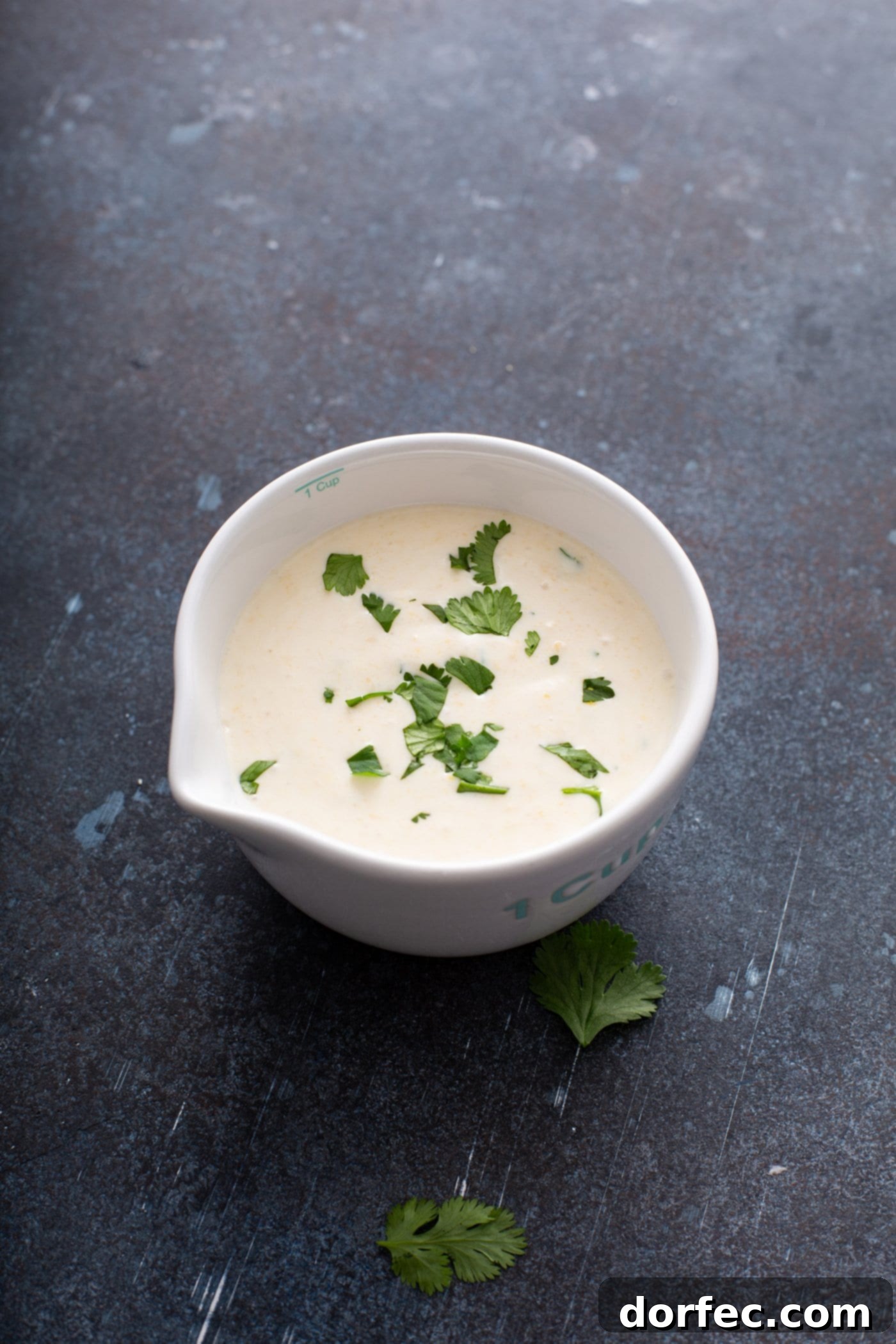 A white bowl showcasing the creamy sweet corn crema, garnished with fresh cilantro leaves. This vibrant and smooth topping is perfect for sweet potato enchiladas, adding a touch of freshness and sweetness to the healthy Mexican dish.