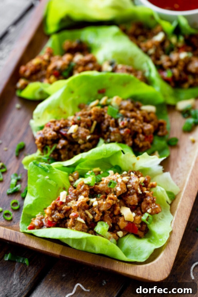 A top-down view of several saucy Thai peanut turkey lettuce wraps, garnished with green onions and slivered almonds.