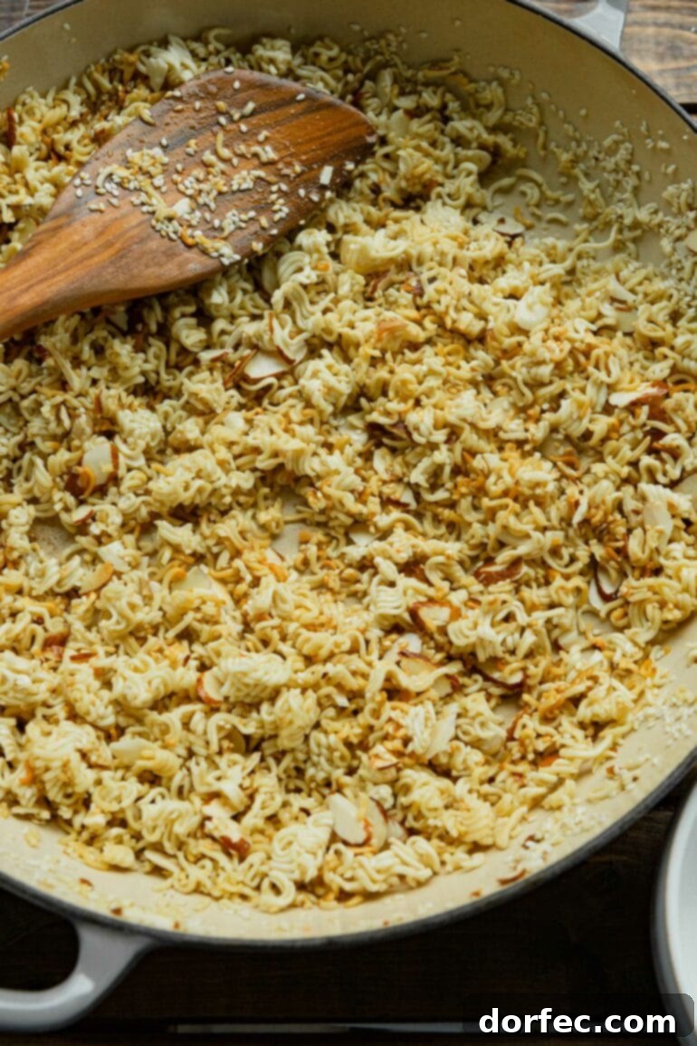 a photo of crushed up ramen noodles being toasted in a shallow dutch oven.