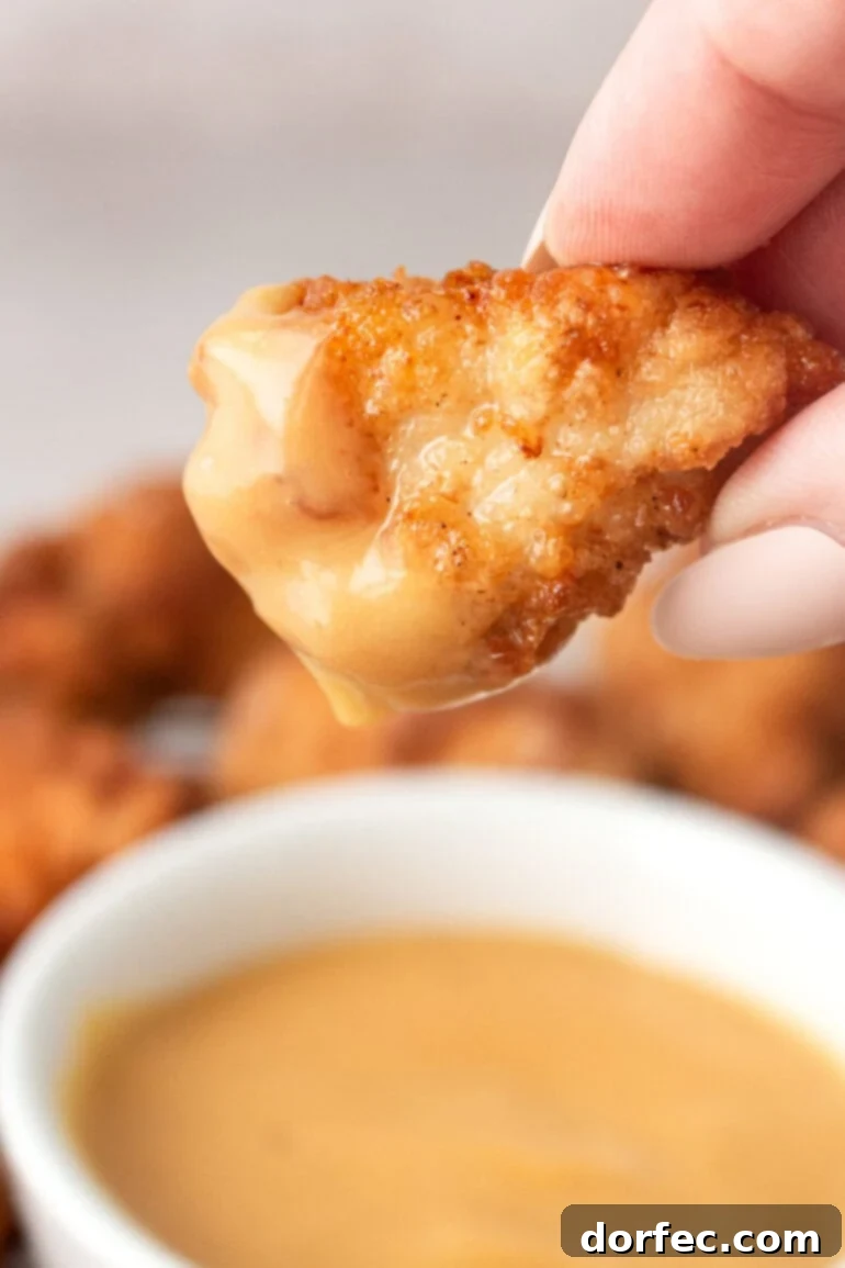 Homemade Chick-Fil-A Style Nuggets and Signature Sauce 3 A golden crispy chicken nugget, perfectly fried and dipped into a creamy, orange-hued sauce, showcasing its delicious texture.
