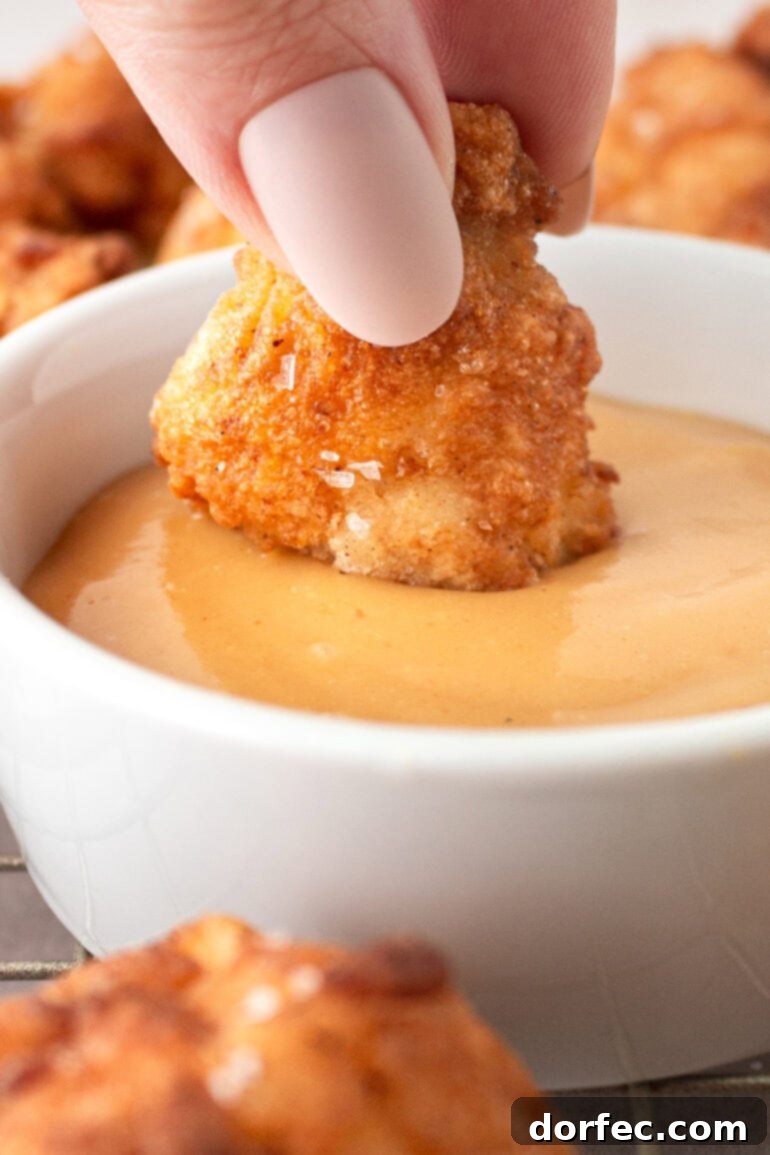 Homemade Chick-Fil-A Style Nuggets and Signature Sauce 7 Someone dipping a golden crispy chicken nugget into a creamy, orange-colored dipping sauce, highlighting the perfect crunch and texture.