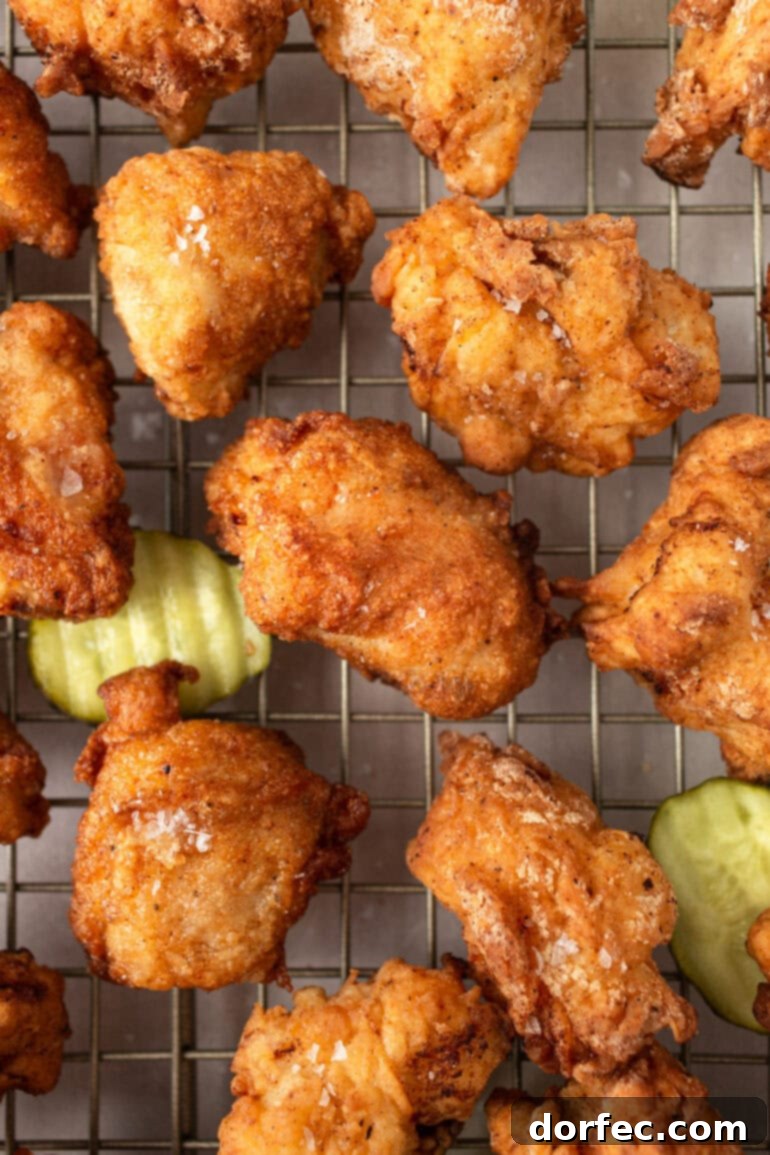 Homemade Chick-Fil-A Style Nuggets and Signature Sauce 8 Several golden deep-fried chicken nuggets resting on a wire cooling rack, with a few dill pickle chips scattered around, emphasizing the pickle brine inspiration.