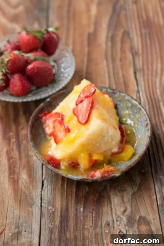Close-up of a slice of Angel Food Cake topped with a generous pour of mango sauce and fresh strawberries, highlighting its fresh appeal.