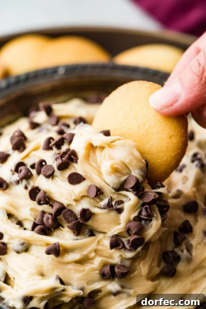 Edible Chocolate Chip Cookie Dough Dip 2 A metal bowl filled with easy chocolate chip cookie dough dip, with a vanilla wafer scooping some up, ready to be enjoyed.