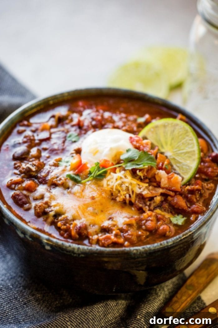 Championship Instant Pot Chili 4 a photo of a bowl full of hearty chili topped with melting cheddar cheese, fresh cilantro, bacon crumbs, a slice of lime and a scoop of sour cream.
