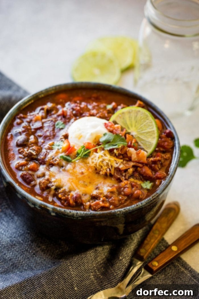 Championship Instant Pot Chili 7 a photo of a bowl full of classic chili loaded with beans, ground beef, and bacon and topped with shredded cheese, sour cream, cilantro and a slice of lime.