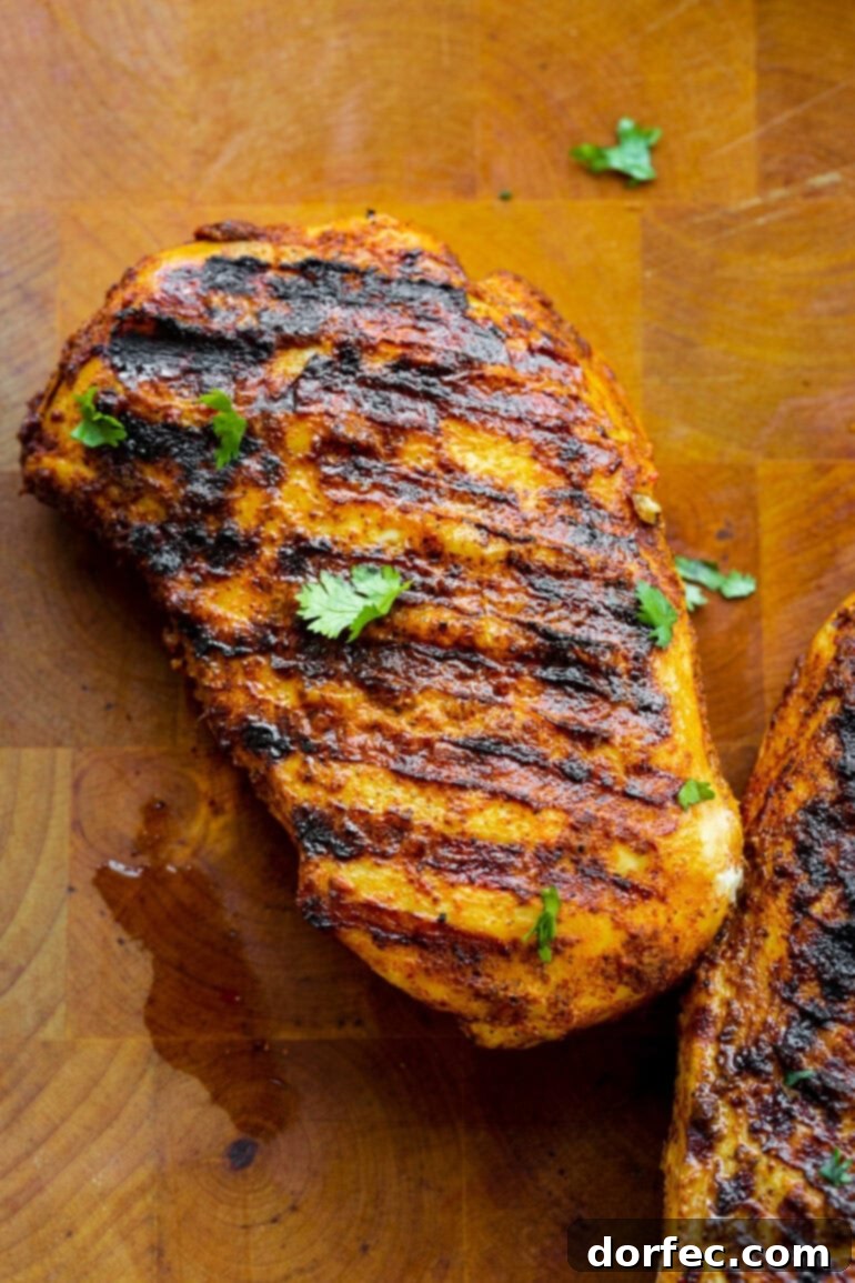 a photo of a grilled seasoned chicken breast sitting on a wooden cutting board