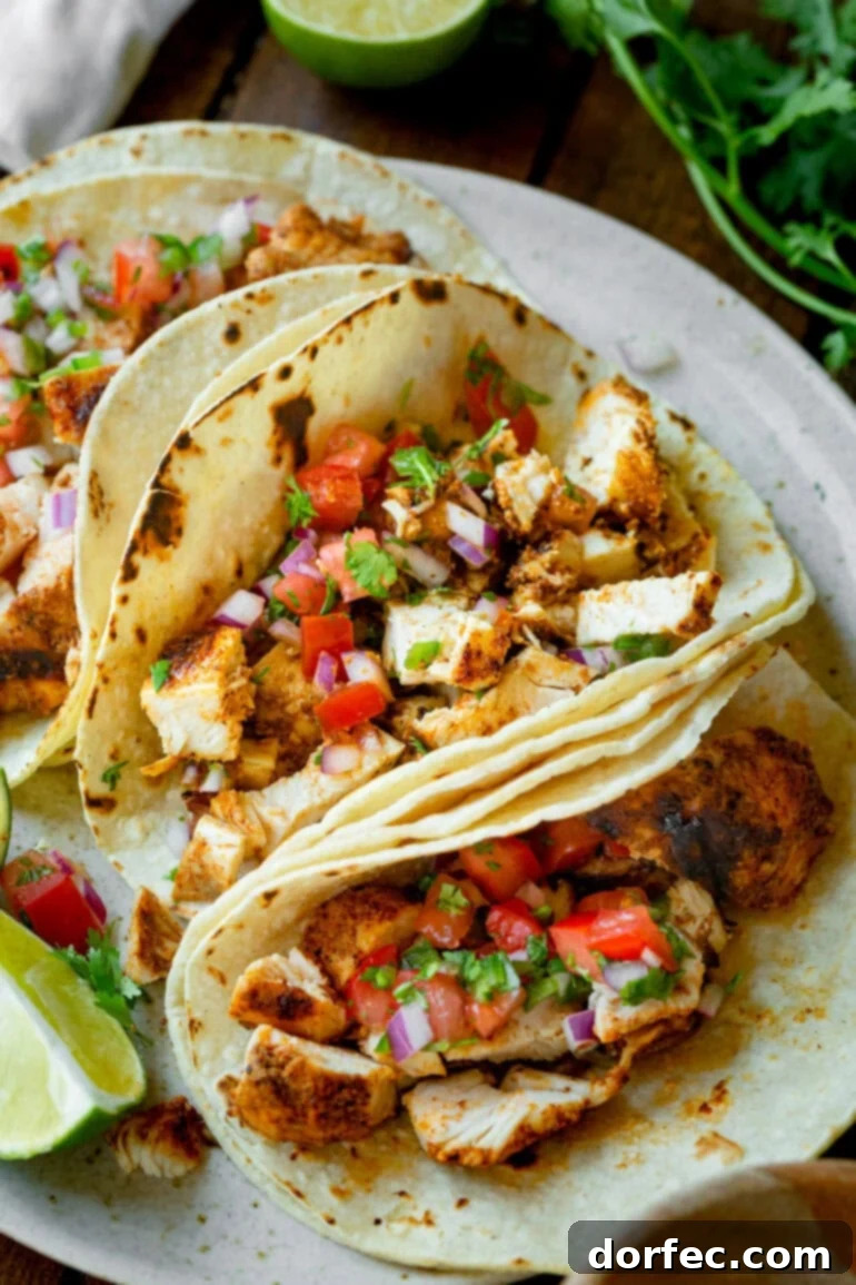 a photo of three grilled chicken tacos sitting on a serving platter in corn tortillas and topped with fresh pico de gallo