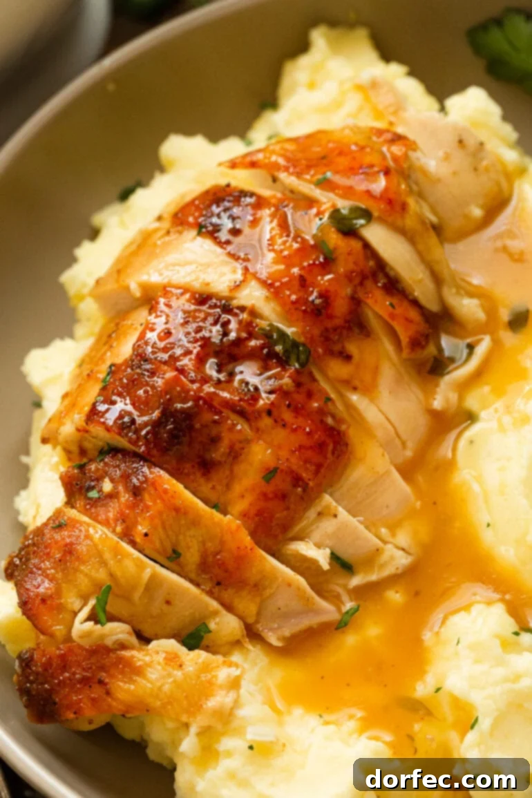 A photo of a golden roasted chicken breast that has been sliced, sitting on top of creamy mashed potatoes covered in rich gravy.