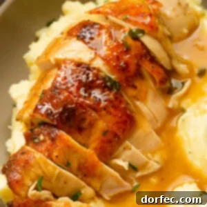 A photo of a golden roasted chicken breast that has been sliced, sitting on top of mashed potatoes covered in gravy.