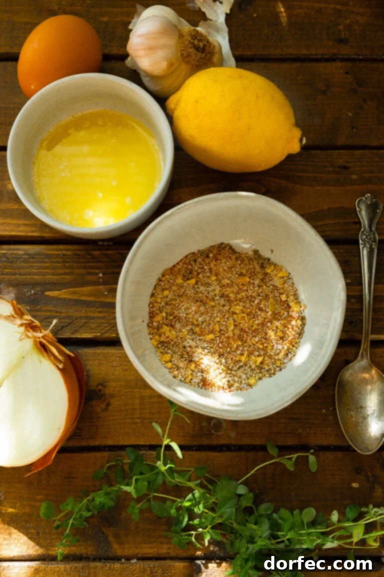 A photo of all the ingredients for a whole roasted chicken in separate small bowls, including a whole lemon, seasonings, half an onion, melted butter, and fresh herbs.