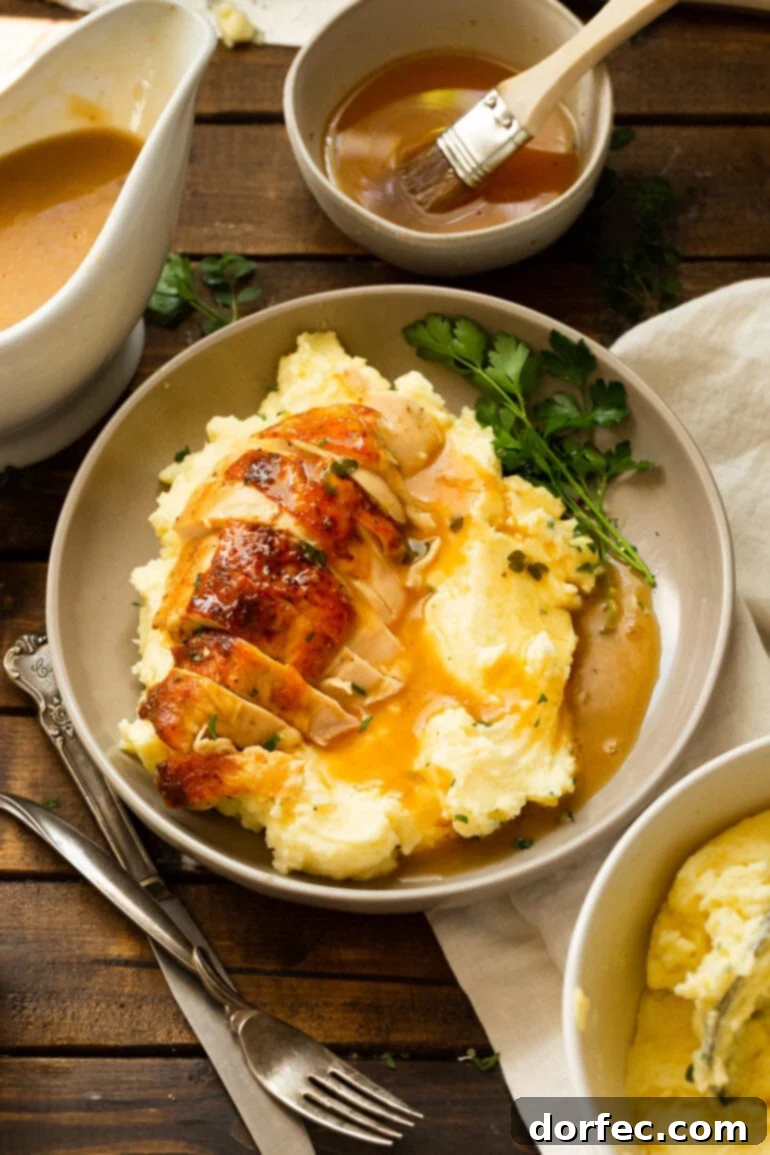 A photo taken over the top of a dinner plate that has a serving of mashed potatoes and gravy on it, topped with a sliced honey roasted chicken breast with some fresh parsley on the side as garnish.