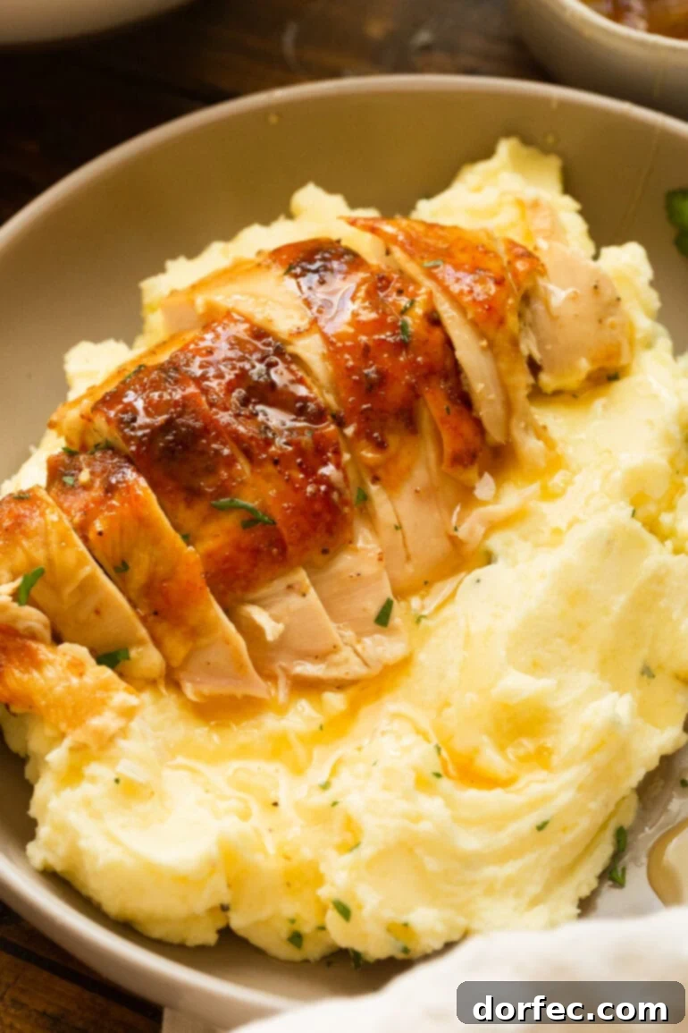 A photo of a golden roasted chicken breast sliced and sitting on top of a serving of creamy mashed potatoes and gravy.