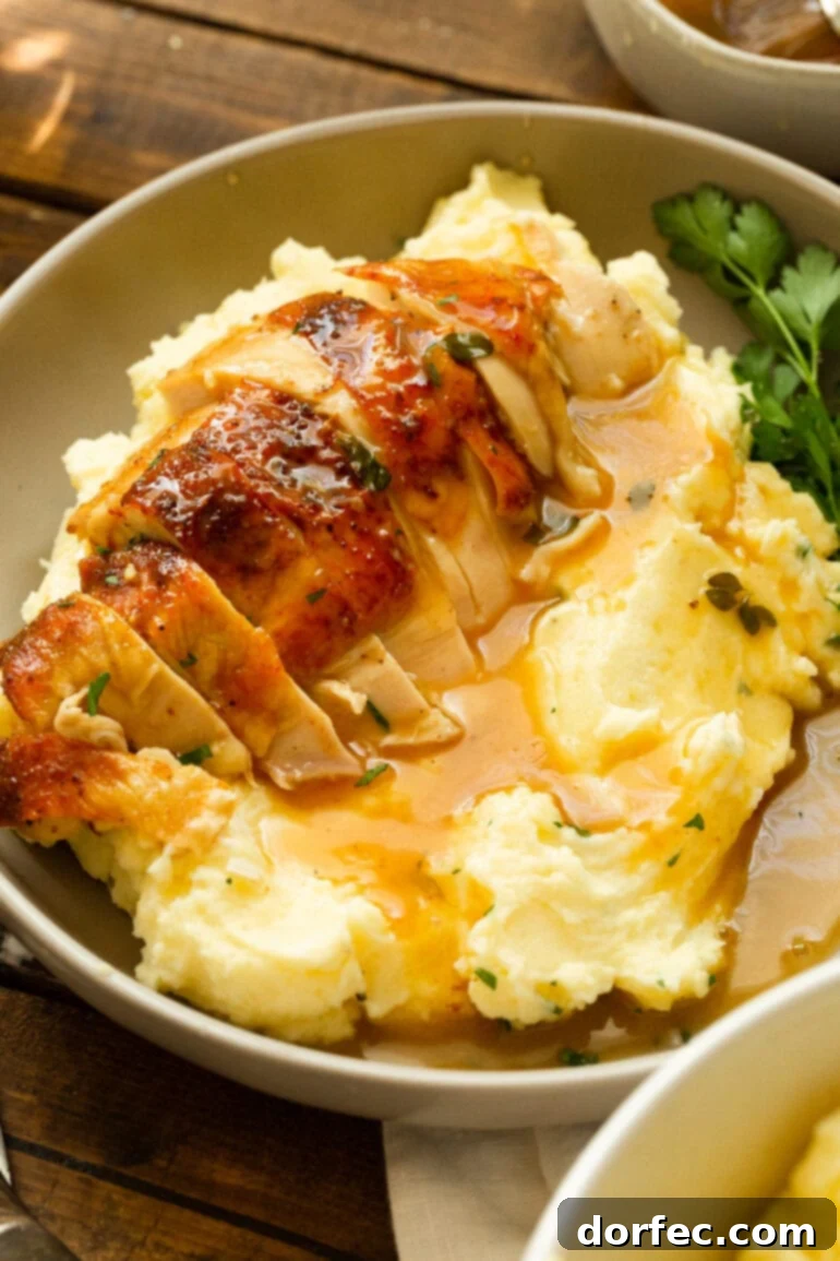 A photo of a serving of creamy mashed potatoes topped with gravy and golden roasted chicken breast that has been sliced.