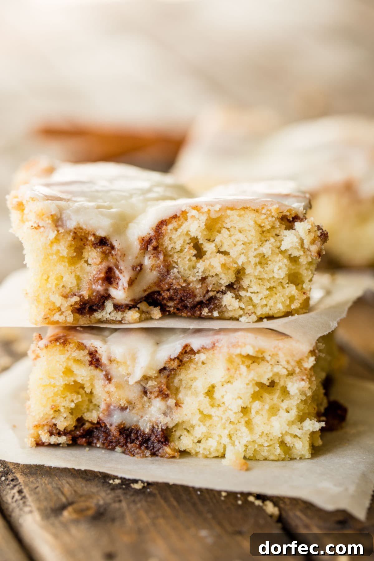 A generous serving of Cinnabon Cinnamon Roll Sheet Cake, glistening with creamy, cooked vanilla cream cheese frosting.