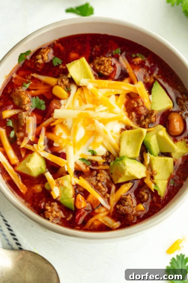 Close-up of taco soup in a grey bowl, garnished with avocado slices, shredded cheese, sour cream, and fresh cilantro.