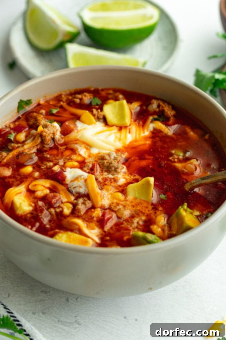 Grey bowl of Instant Pot taco soup on a white countertop, topped with fresh cilantro, sour cream, shredded cheese, and sliced avocado.