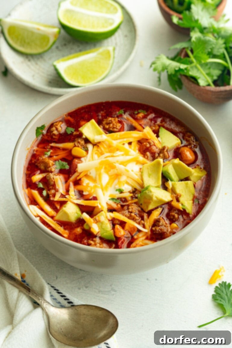 a bowl of taco soup topped with shredded cheddar cheese, sour cream and diced avocado